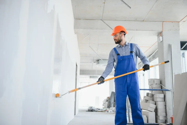 A painter in a blue uniform paints the wall with a long rolling pin.