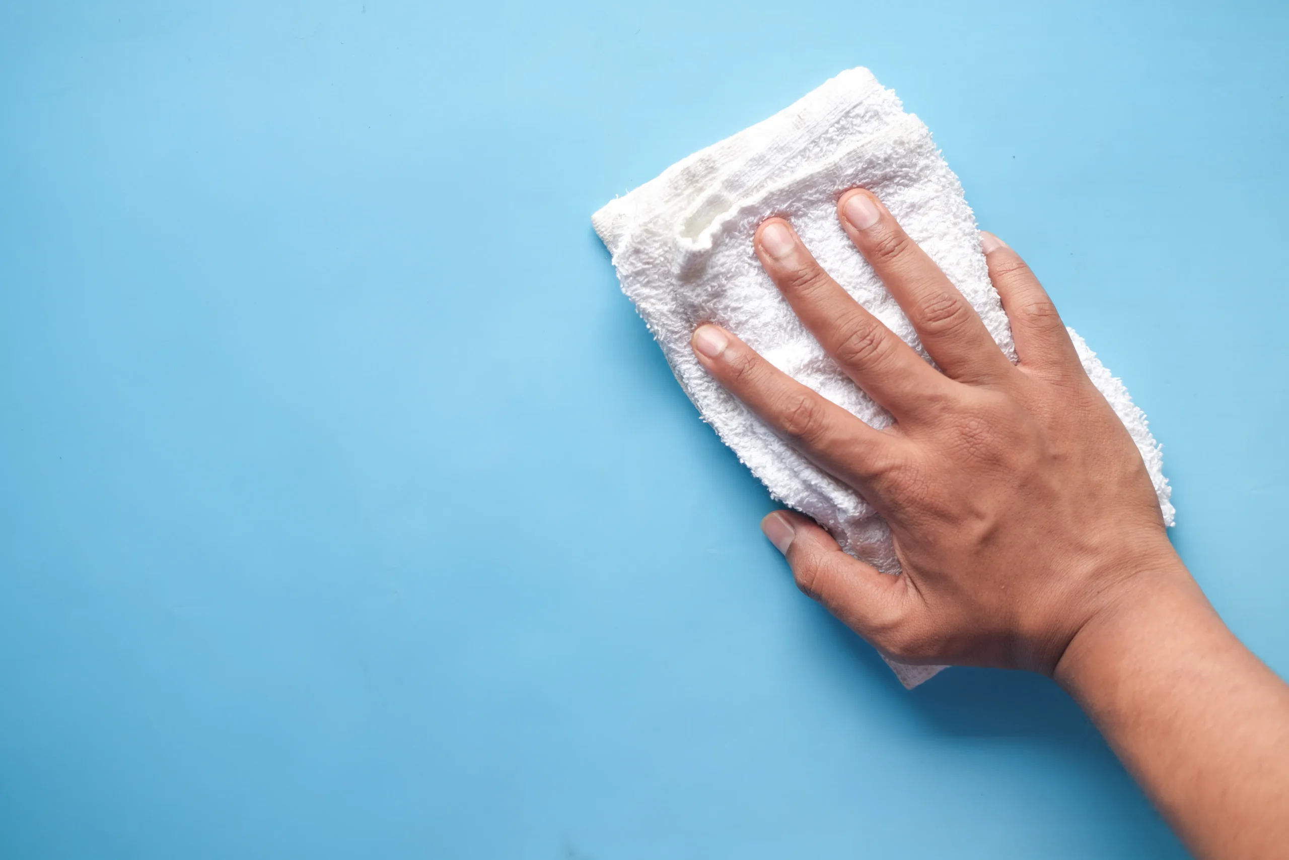 Closeup image of a person gently cleaning a wall with soft cloth, demonstrating proper painting maintenance.